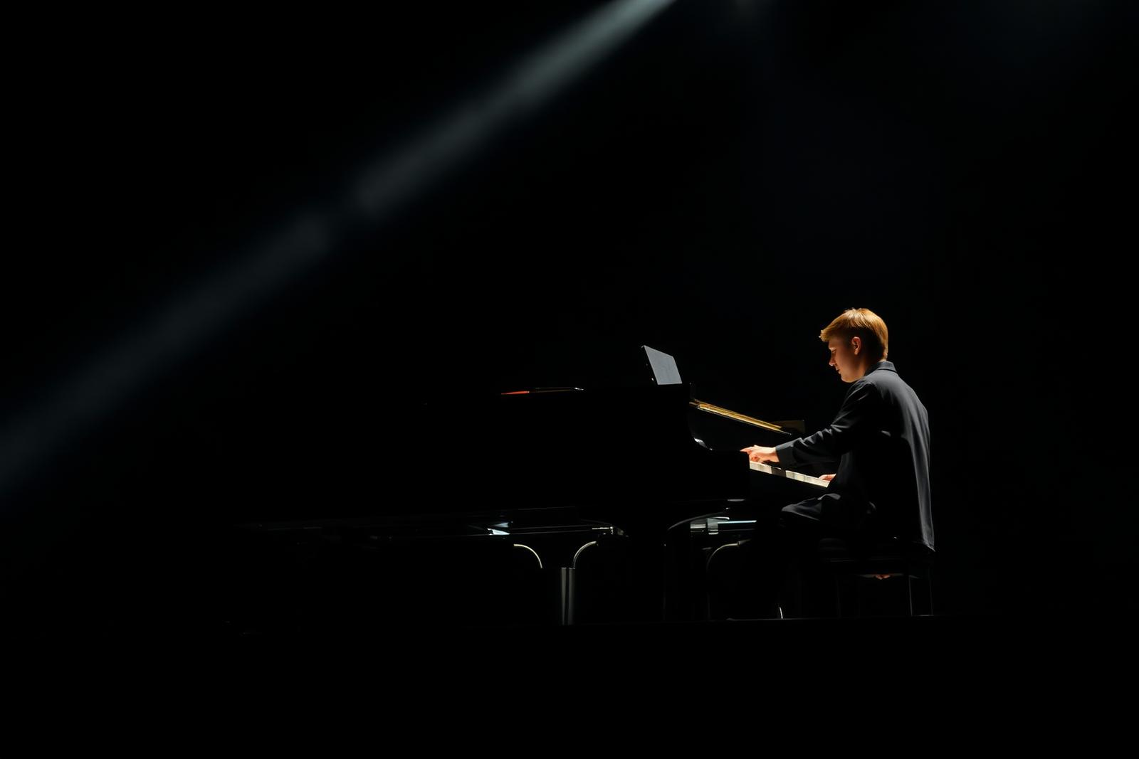 Student pianist performing on stage under a spotlight